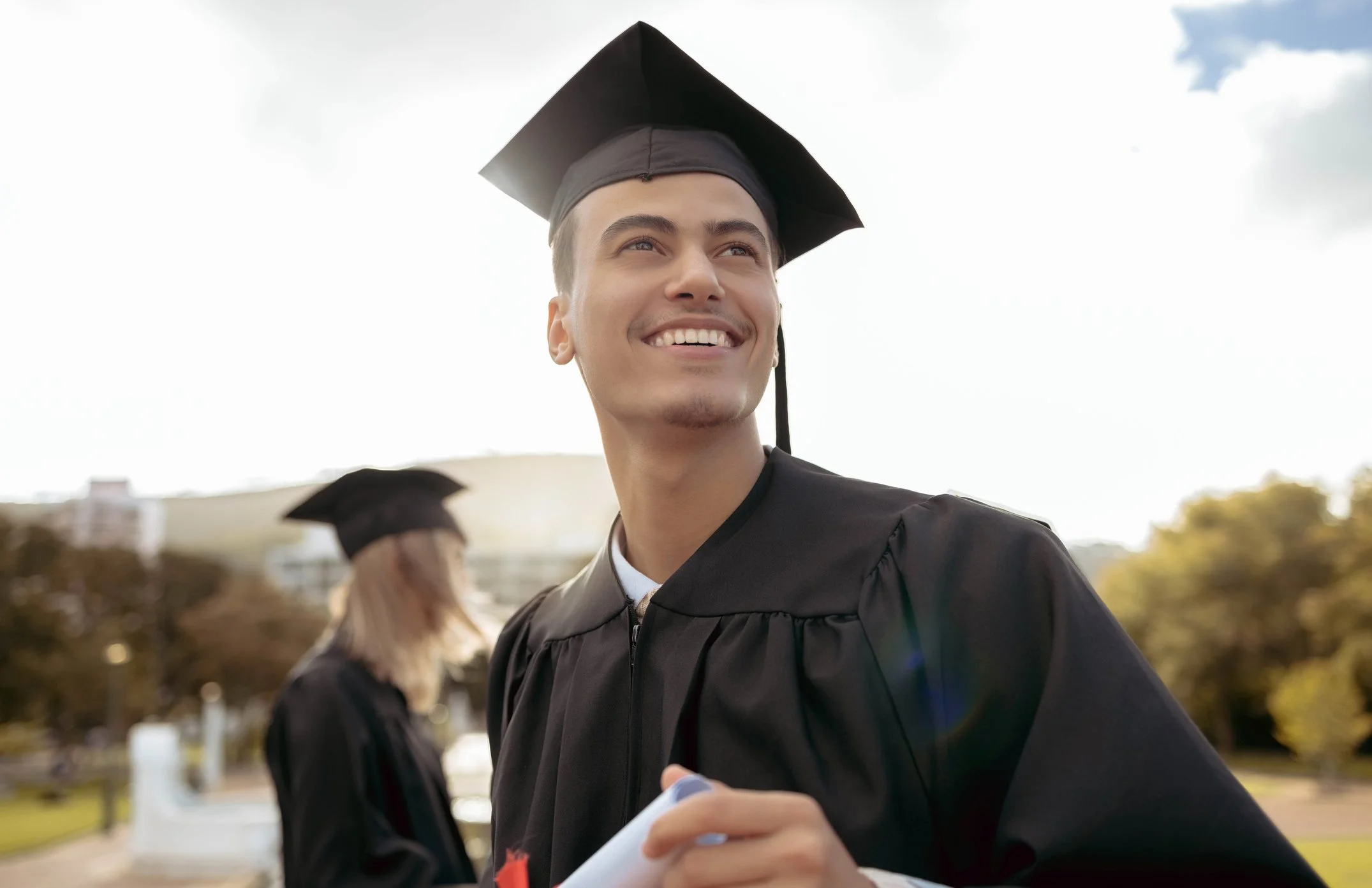 Male student in graduation cap and gown smiling after college acceptance, celebrating success with college coaching guidance